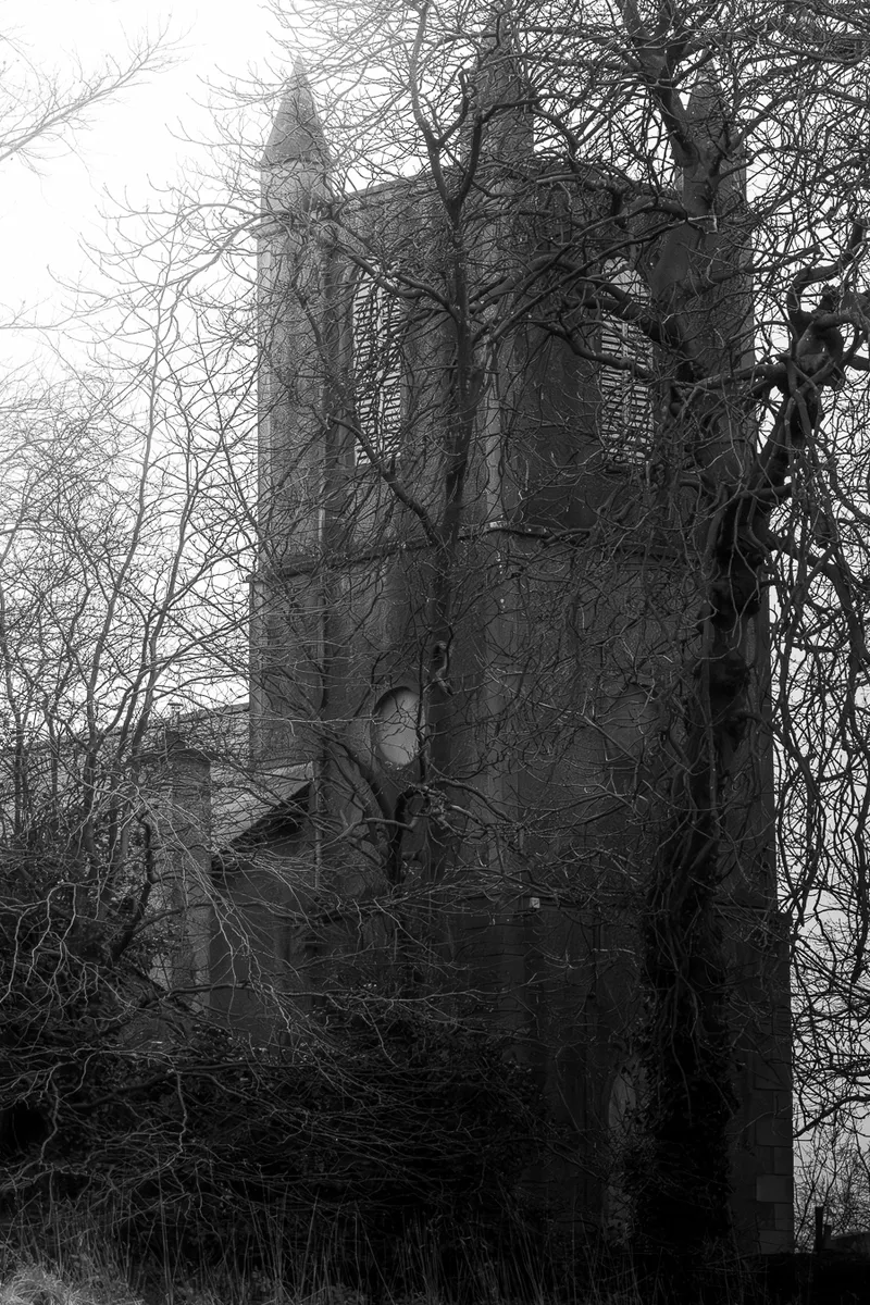 Abandoned church tower behind bare winter trees, black and white